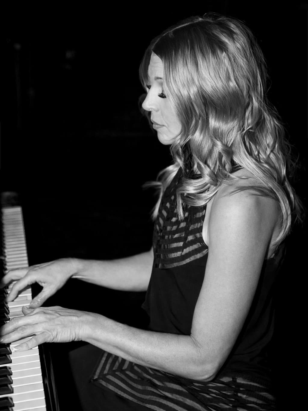 Lisa Apple playing piano in profile against a dark backdrop